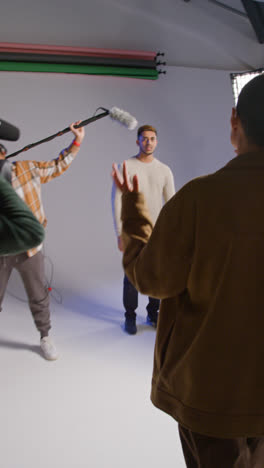 Vertical-Video-Of-Frustrated-Female-Assistant-And-Director-With-Clapperboard-As-Actors-Shoot-Movie-Or-Video-In-Studio-With-Film-Crew-And-Director-Shot-In-Real-Time